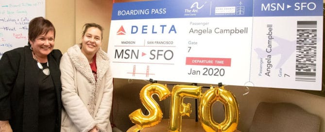 Two women standing next to large Delta boarding pass