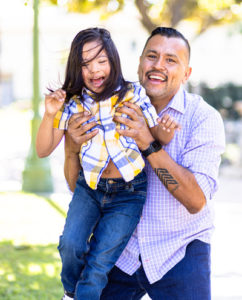 A smiling father holds up his laughing son, who has Down syndrome.